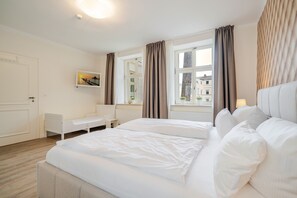 Hotellihuone, jossa on sänky, työpöytä, tuoli, ikkuna verhoilla ja taulu seinällä.