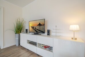 Un salon moderne avec un téléviseur à écran plat, une plante en pot, une lampe et une étagère où sont exposées des voitures miniatures.