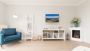 A modern living room with a blue sofa, white shelving unit, a flat-screen TV, and a fireplace. - Haus am Schmollensee, app. 7h (Heringsdorf)