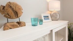 A white console table with a wooden fish sculpture, two blue glass cups, a framed photo, and a lamp. - Haus am Schmollensee, app. 7h (Heringsdorf)