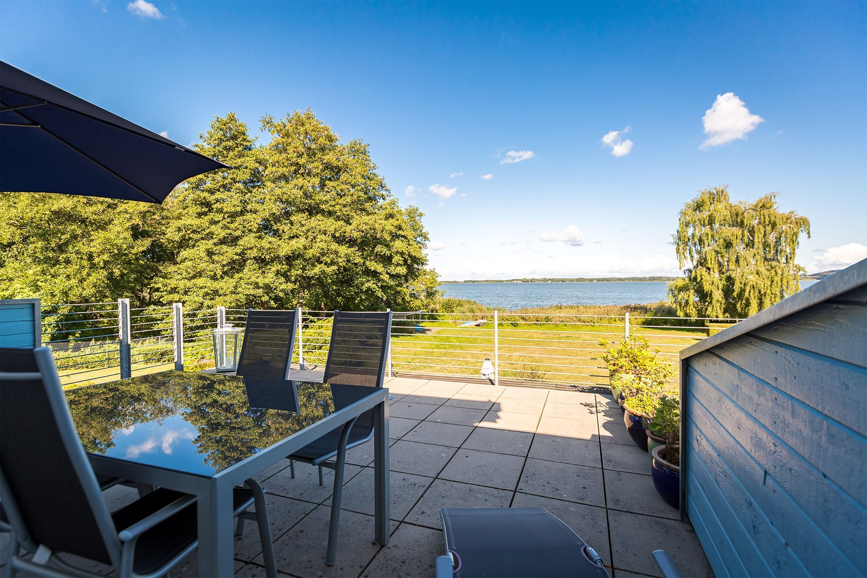 Une terrasse avec une table et des chaises, une vue sur le lac et des plantes en pot.