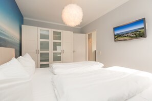 Quarto com cama, guarda-roupa branco e televisão na parede.