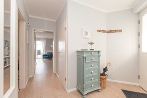 Um corredor com uma cômoda azul-clara, uma cesta de vime e uma prateleira de madeira na parede.