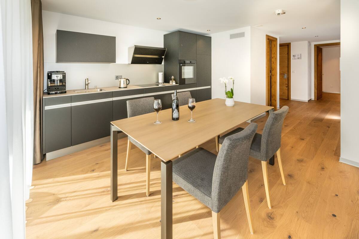 A modern kitchen with a built-in oven and a dining area with a wooden table and grey chairs.