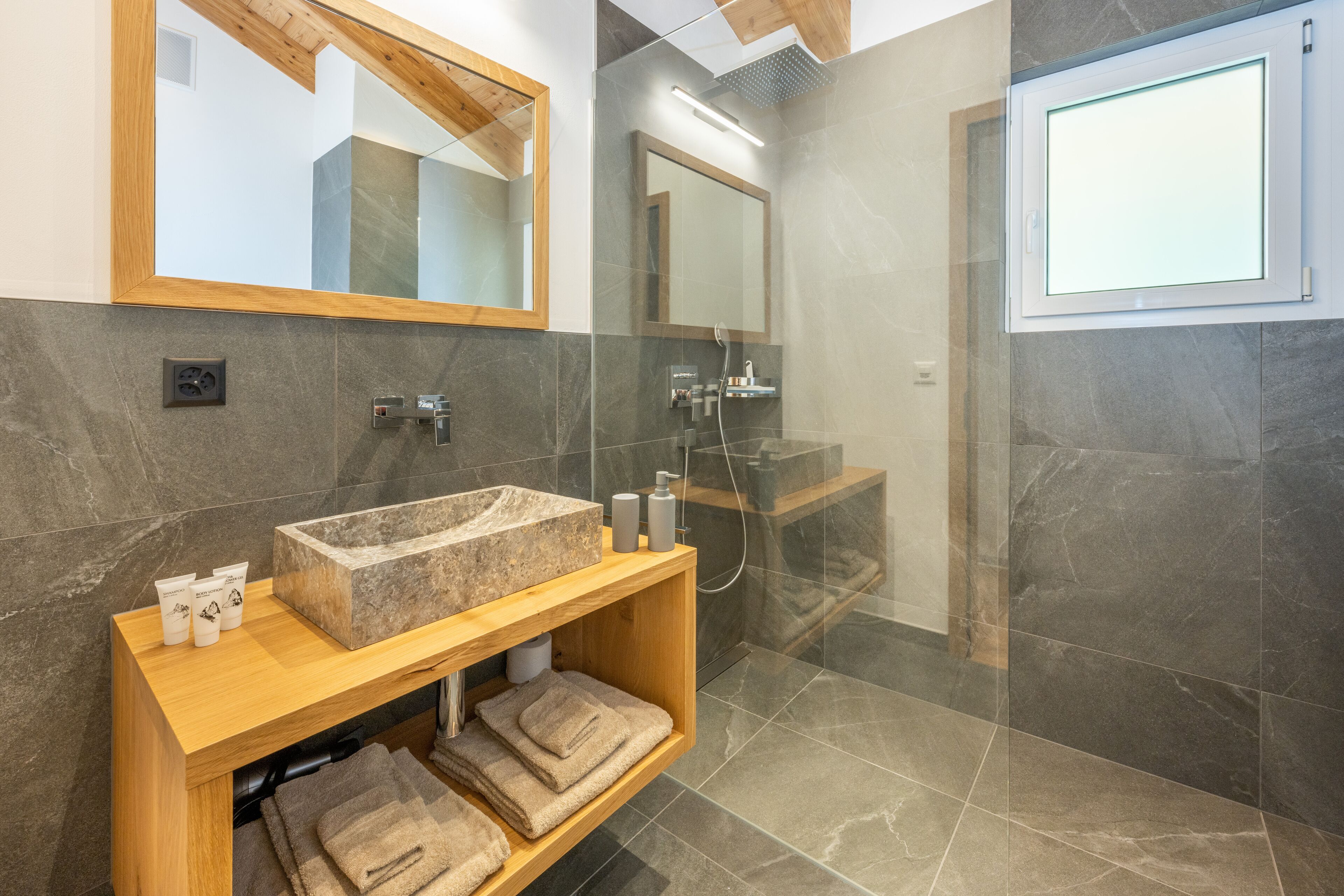 Une salle de bain moderne avec un grand miroir, un meuble-lavabo en bois, un vasque en marbre et une cabine de douche en verre.