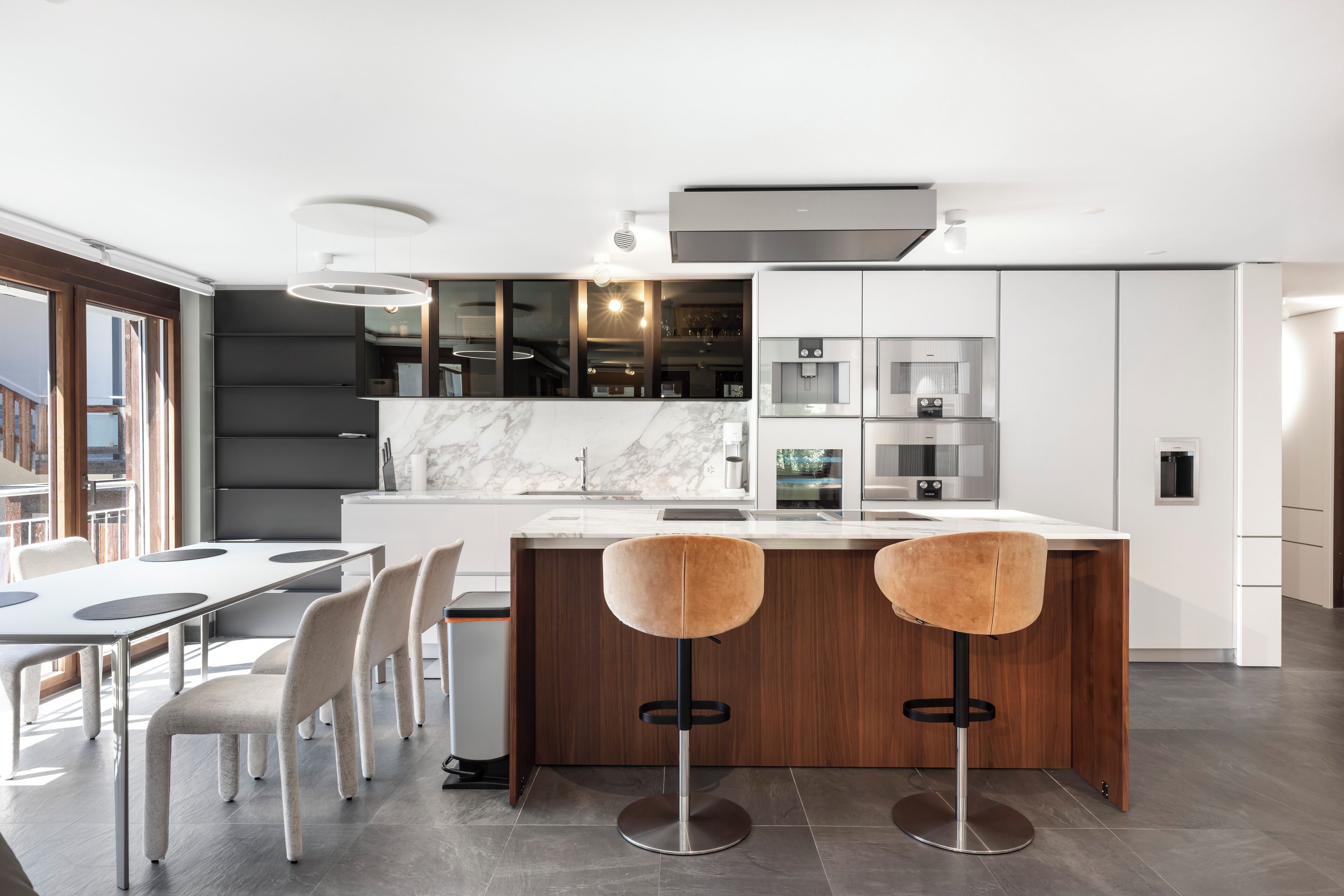 A modern kitchen with a marble countertop, two stools, and a dining area with a table and chairs.