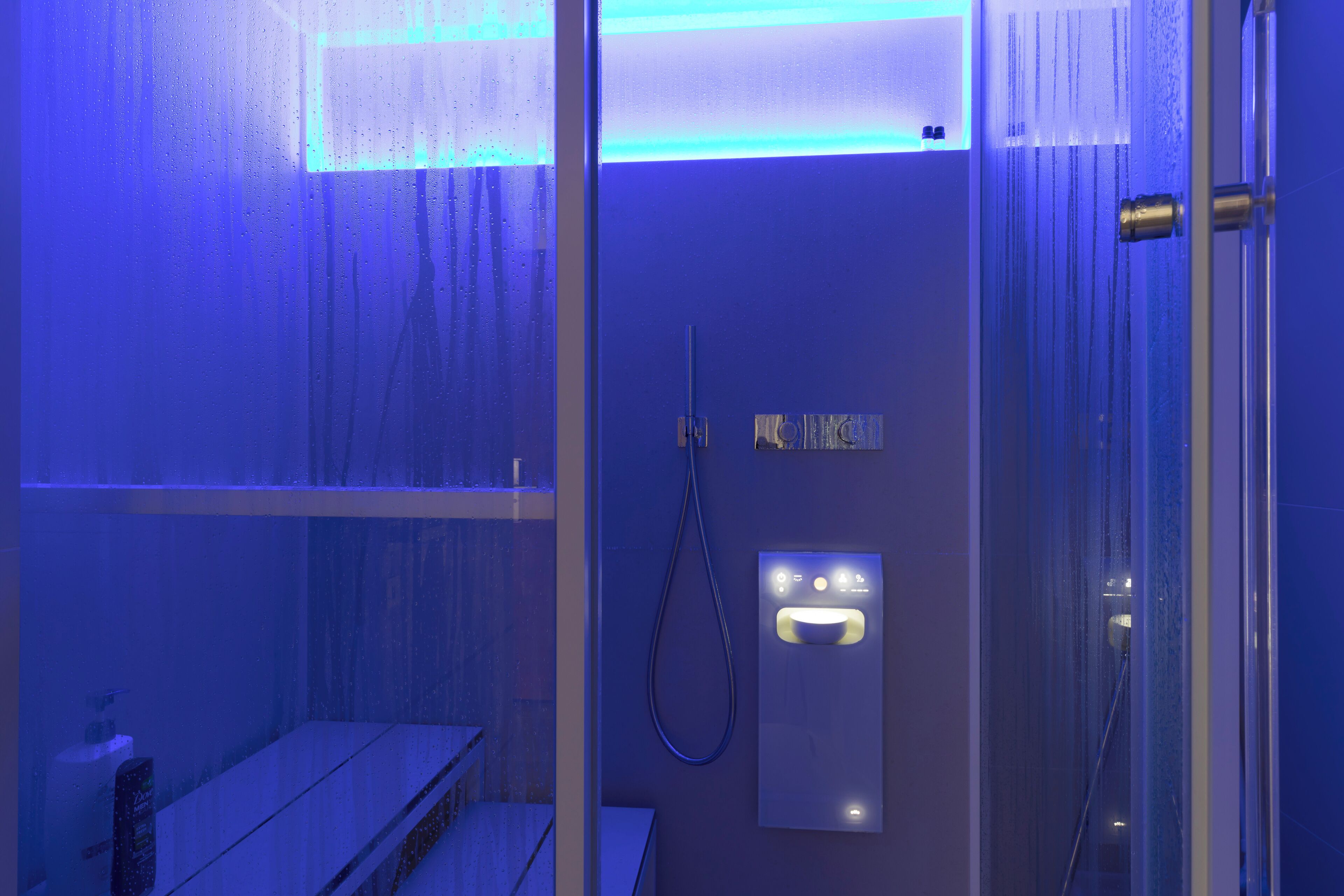 Une salle de bain moderne dotée d’une douche à parois de verre, d’un panneau de commande et d’un banc.