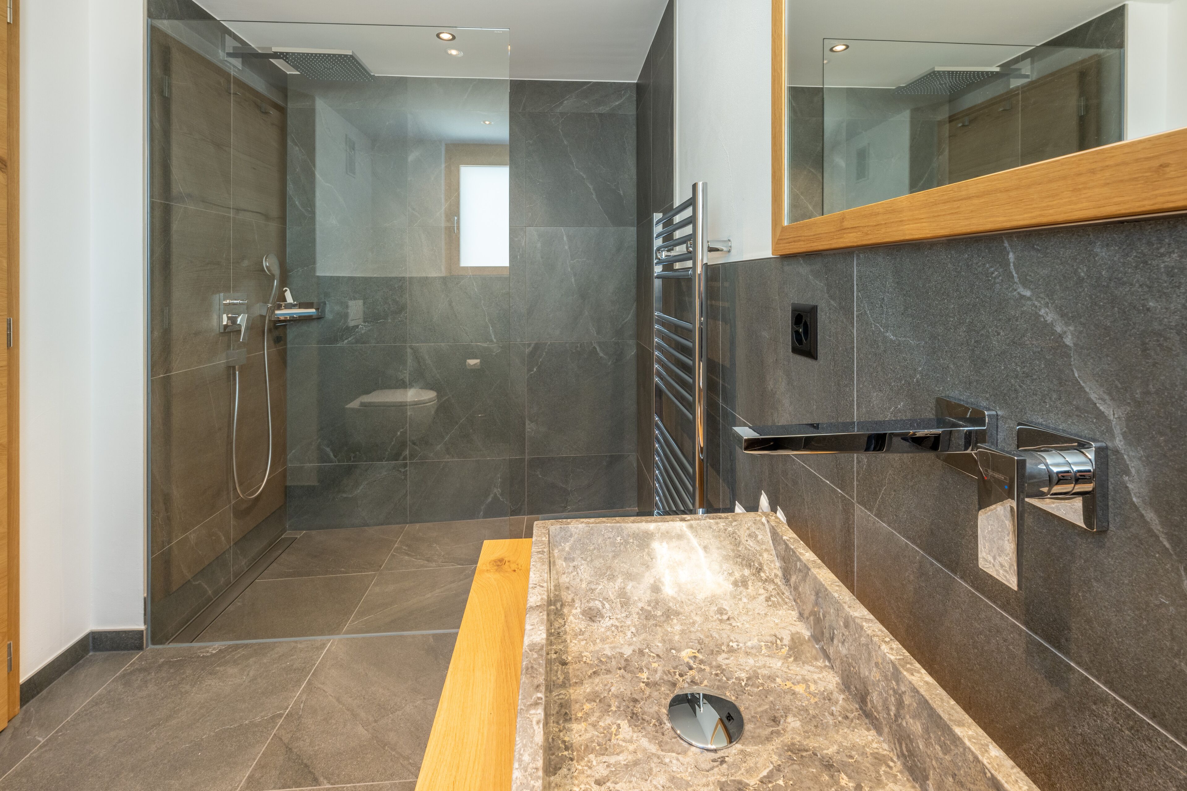 A modern bathroom with a glass-enclosed shower, a wooden vanity, and a large mirror.