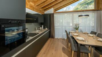 A modern kitchen with a built-in oven, a dining area with a table set for four, and a large window with a mountain view.