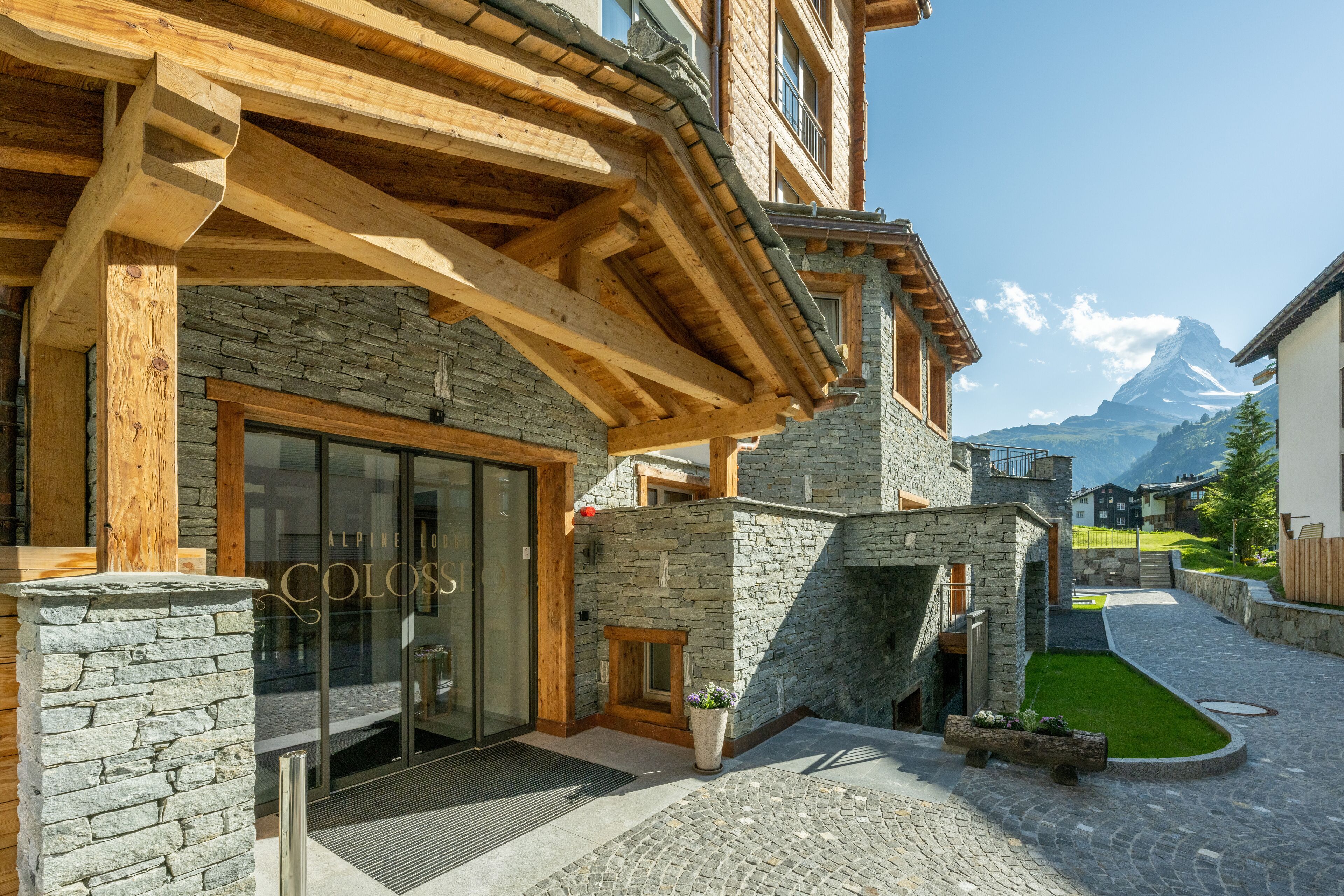 A hotel entrance with stone walls, wooden beams, and a clear view of a mountain in the background.