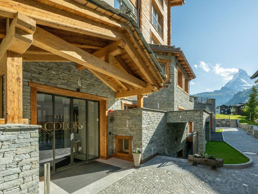 A hotel entrance with stone walls, wooden beams, and a clear view of a mountain in the background.