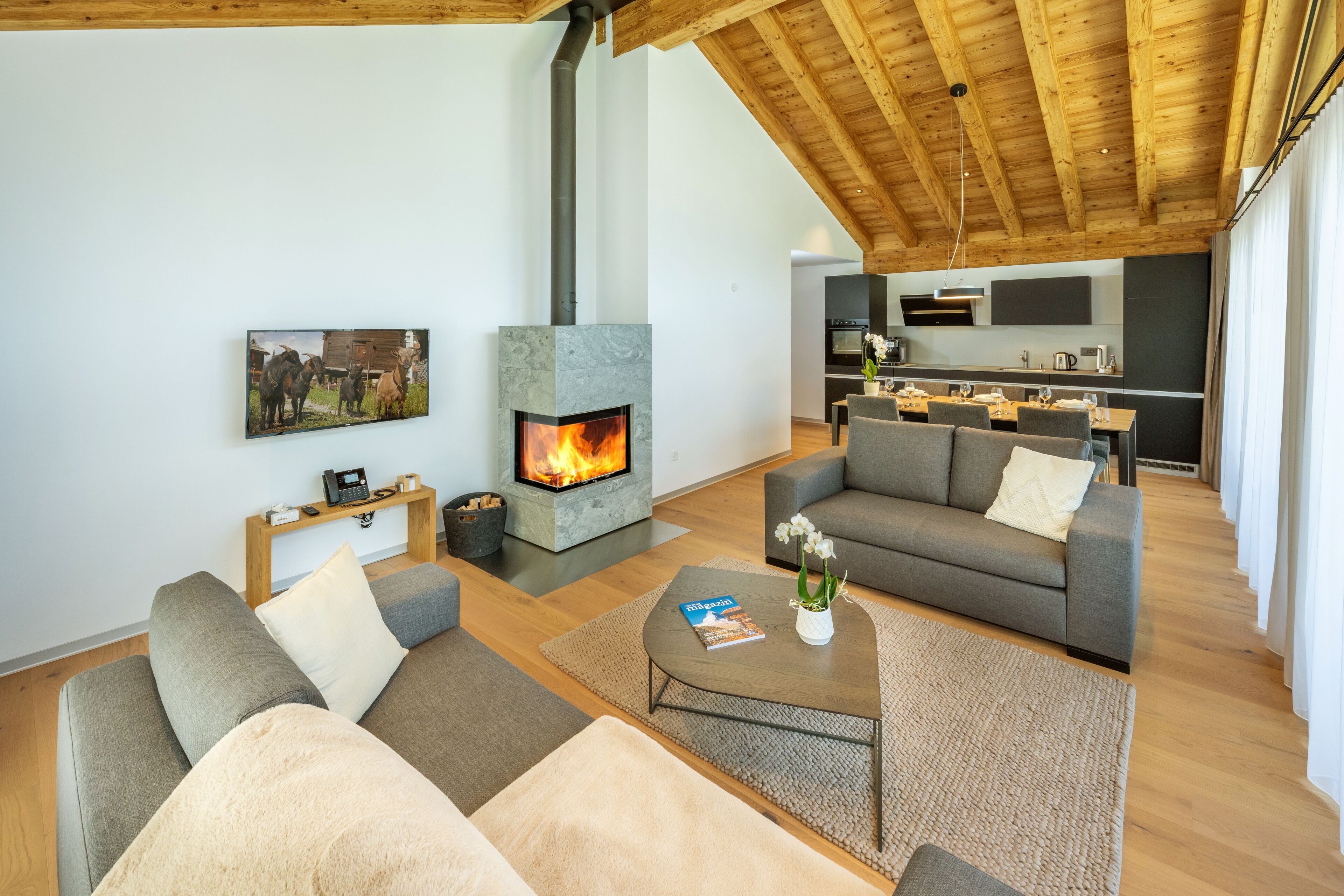 A modern living room with a fireplace, sofas, a coffee table, and a kitchen in the background.