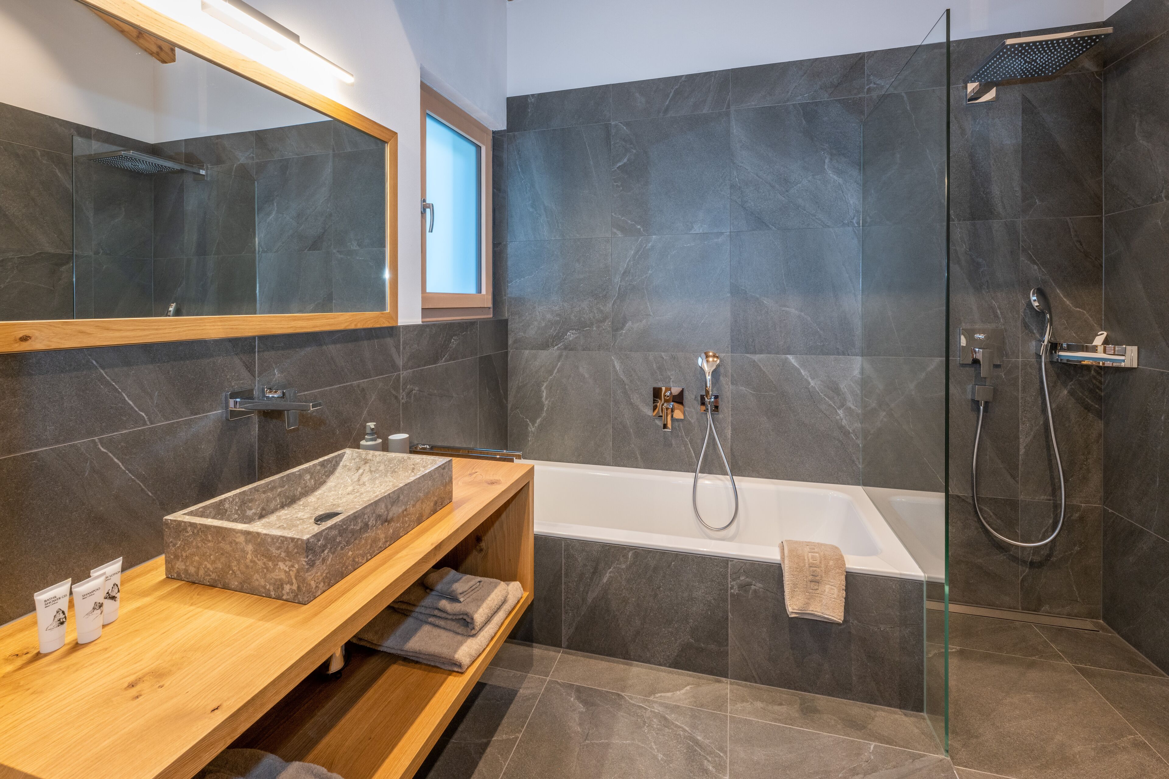 A modern bathroom with a freestanding bathtub, a glass-enclosed shower, and a wooden vanity with a marble sink.