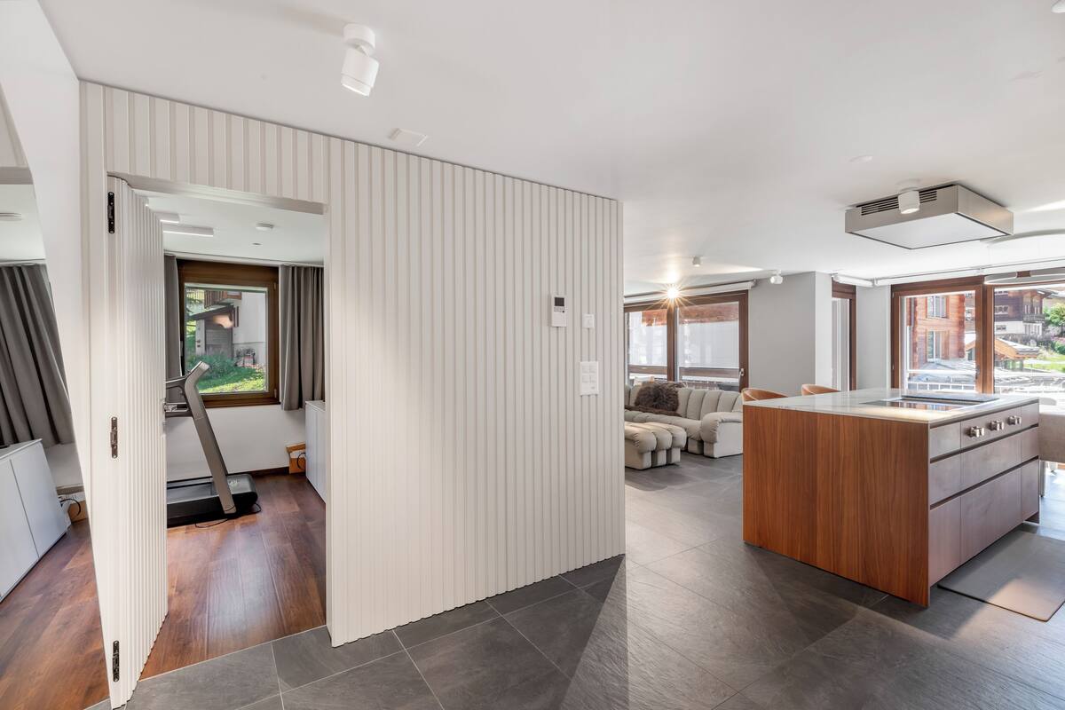 A modern kitchen with a central island, a dining area with a sofa, and a view of the outside.