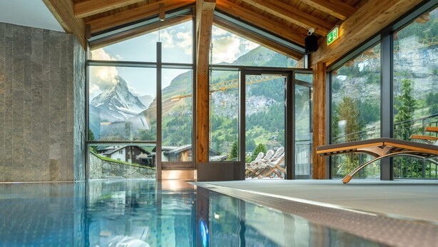 A modern indoor pool with a clear view of mountains and a construction site through large windows. - Luxury Residence Colosseo Zermatt (Zermatt)