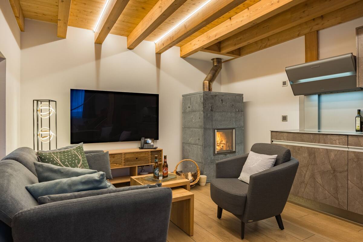 A modern living room with a fireplace, a flat-screen TV, and a wooden ceiling.