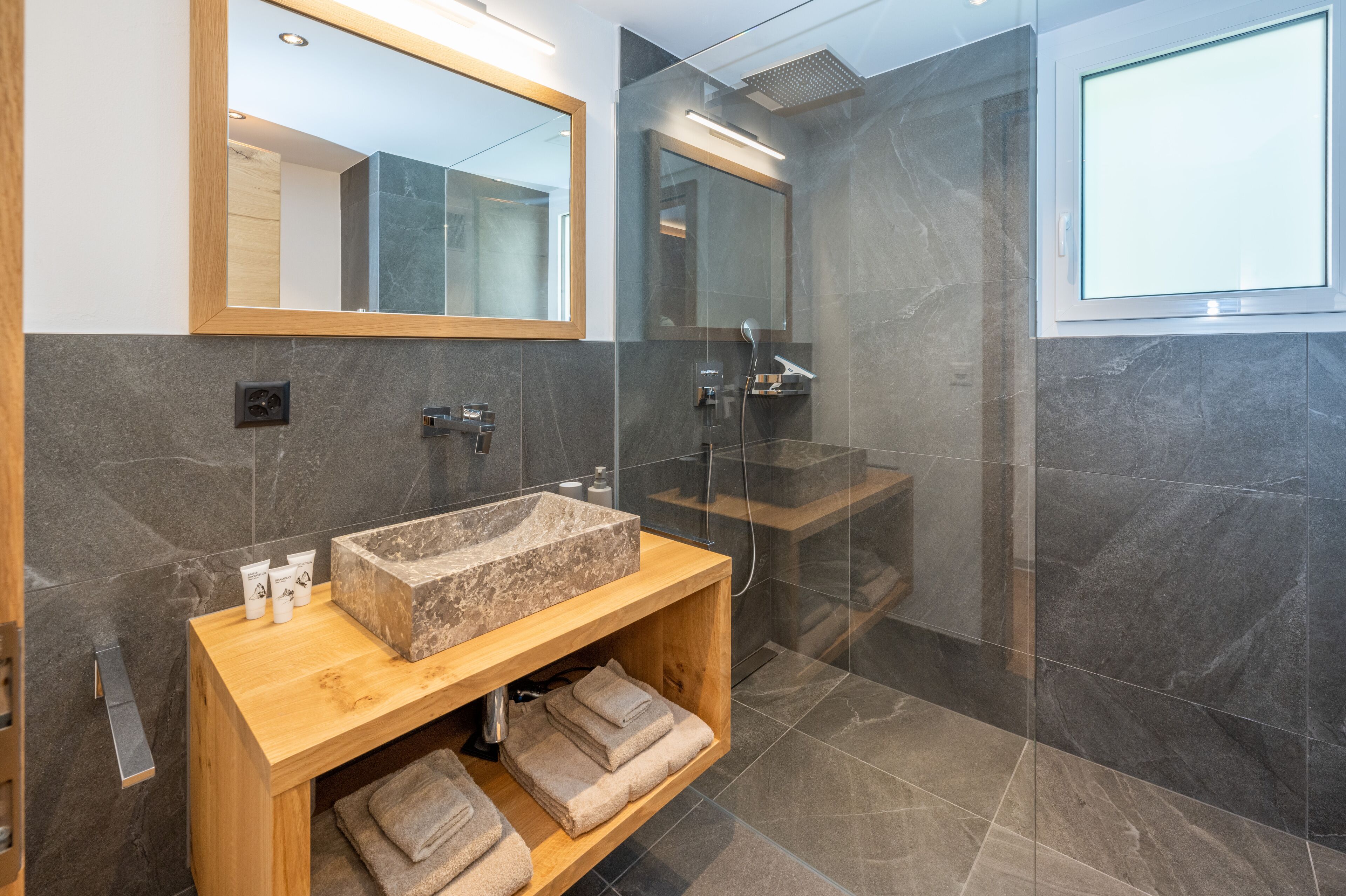 A modern bathroom with a large mirror, a wooden vanity, a marble sink, and a glass shower enclosure.