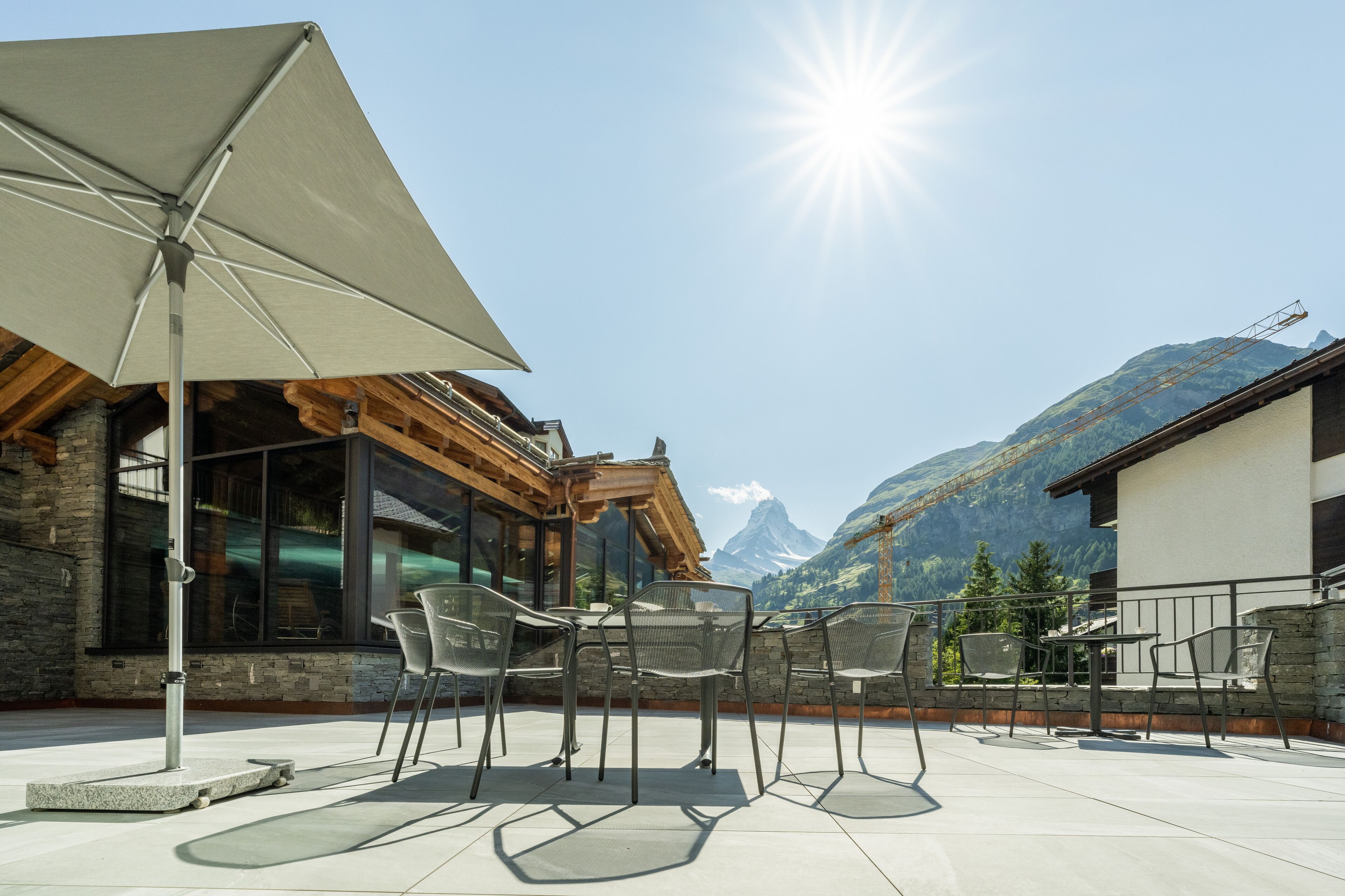 An outdoor patio with chairs and a table, a large umbrella, and a mountain view.
