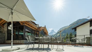 An outdoor patio with chairs and a table, a large umbrella, and a mountain view.