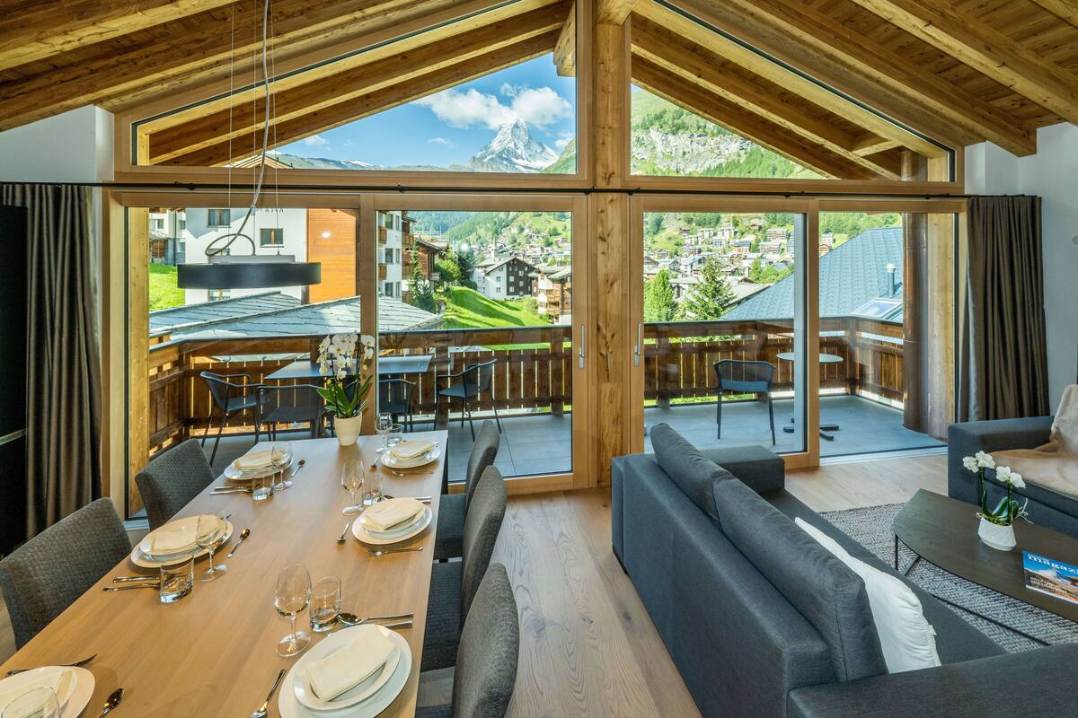A dining area with a wooden table set for a meal, a sofa, and a view of a mountain.