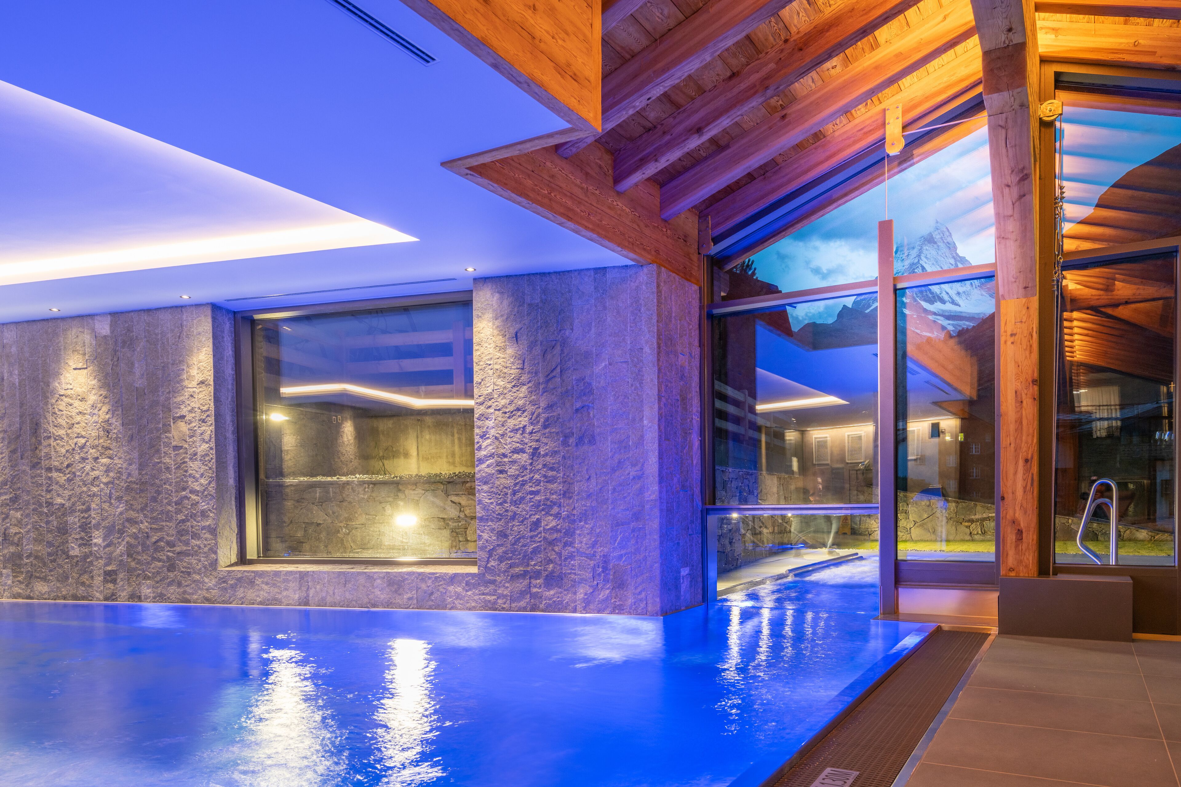 A modern indoor swimming pool with stone walls and large windows.