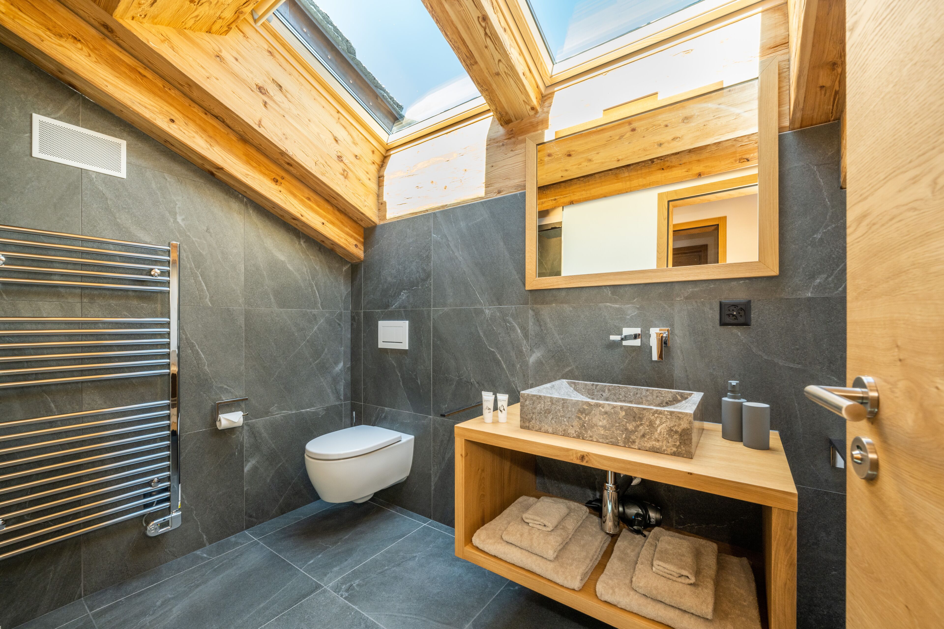 Une salle de bain moderne dotée d’un puits de lumière, d’un meuble-lavabo en bois, de toilettes et d’un porte-serviettes.