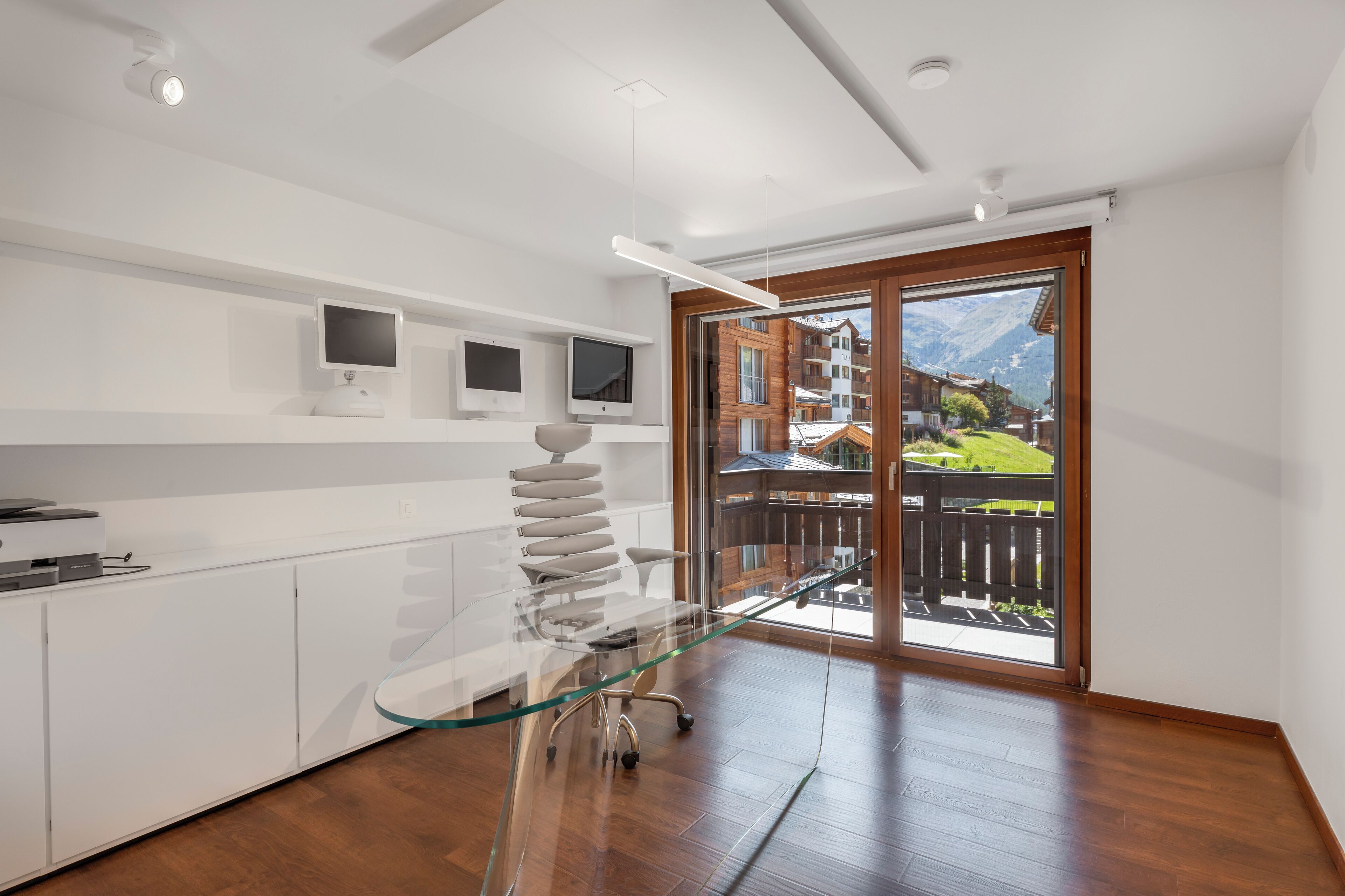 A modern kitchen with white cabinetry, a glass dining table, and a view of a mountain landscape through large sliding glass doors.