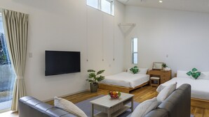 Quarto moderno e bem iluminado, com televisão de tela plana, duas camas, um sofá e uma mesinha.