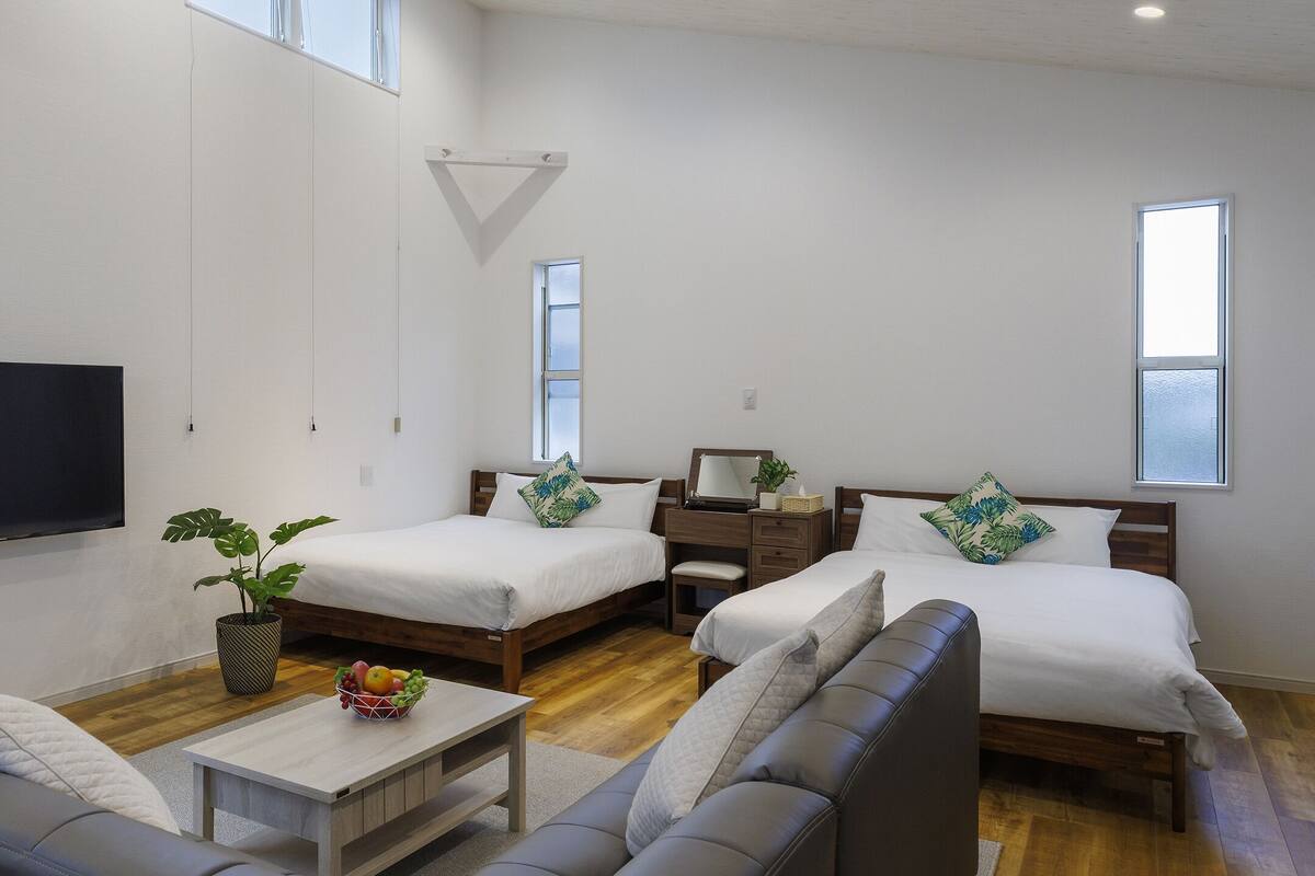 A modern hotel room with two beds, a sofa, a TV, and a small table with fruit.