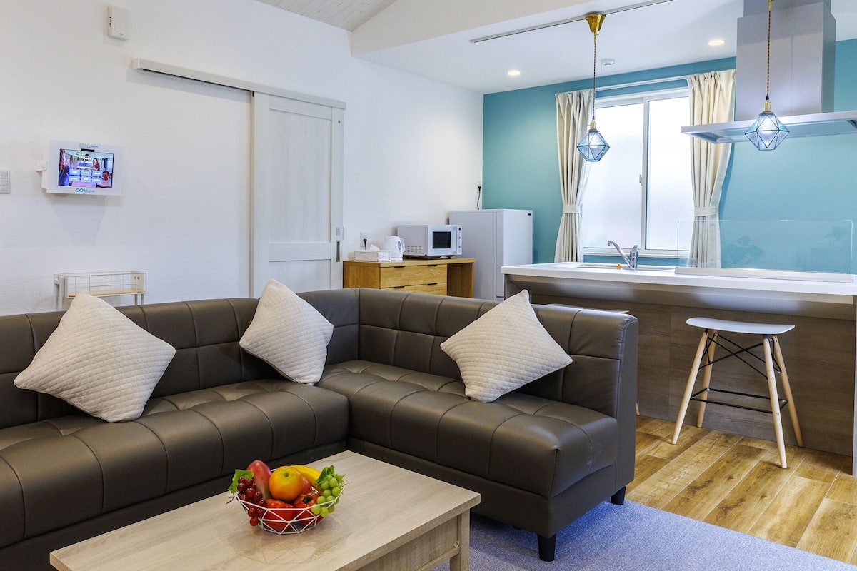 A modern living room with a sectional sofa, a small kitchen area, and a dining table.