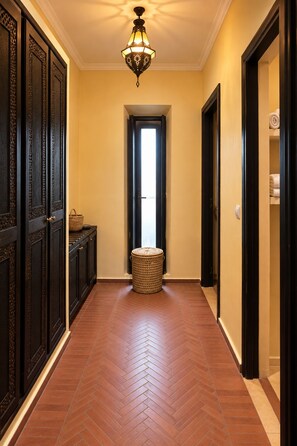 A hallway with a herringbone patterned floor, a woven basket, and a door leading to a room with a towel rack.