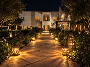A pathway leading to a building with a modern architectural style, surrounded by lush greenery and illuminated by decorative lanterns. - Villa Malaa'ika for 20 people (Marrakech)