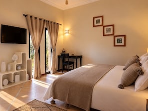 A bedroom with a bed, a desk, a chair, a TV, and a wall-mounted light fixture.