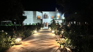 A pathway leading to a building with a modern design, flanked by lit lanterns and greenery. - Villa Malaa'ika for 20 people (Marrakech)