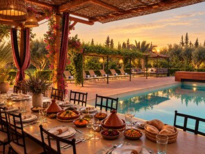 An outdoor dining area with a pool, tables set for a meal, and lounge chairs. - Villa Malaa'ika for 20 people (Marrakech)