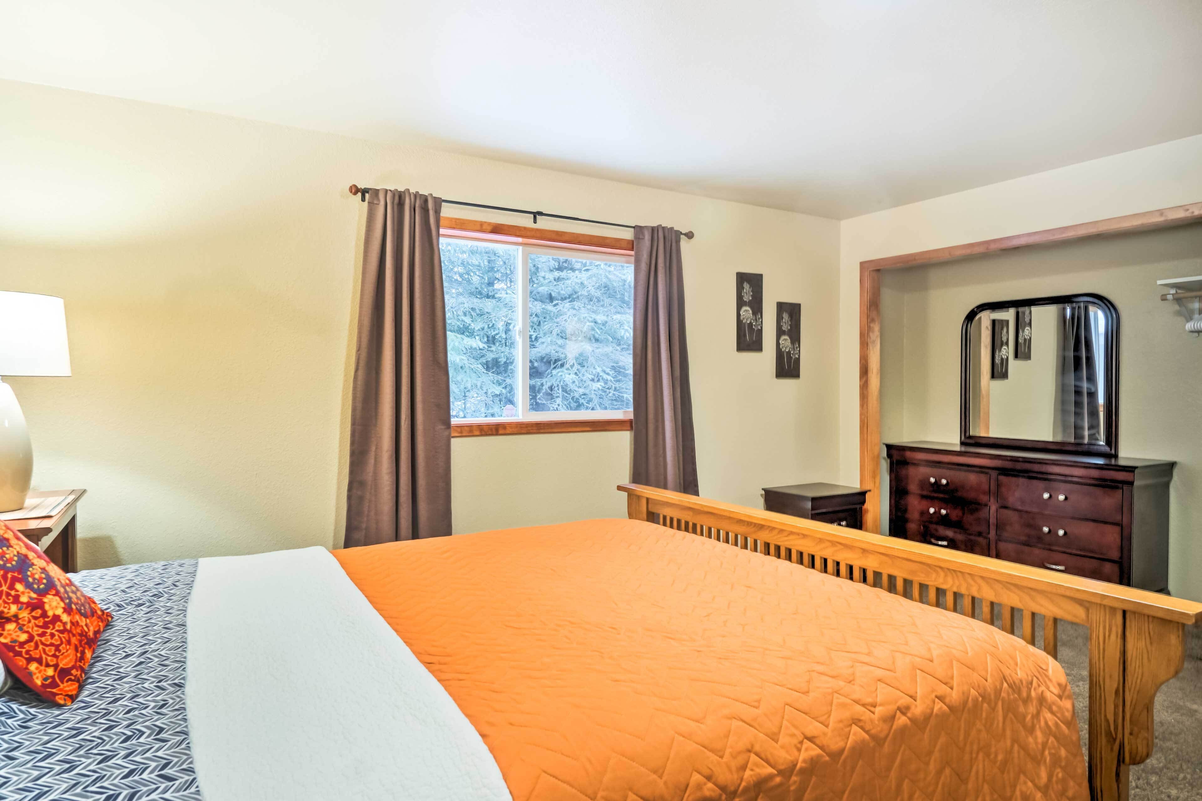 Une chambre à coucher avec un grand lit, une commode, un miroir et une fenêtre avec des rideaux.