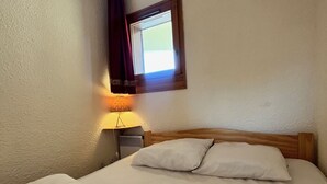Un llit ben fet amb dos almoinos, una làmpada de nit i una finestra amb cortines.
