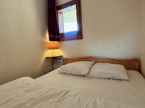 Een keurig opgemaakt bed met twee kussens, een bedlampje en een raam met gordijnen.