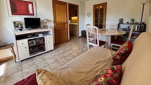 Un espai habitable pràctic amb llit, escriptori i ordinador, taula de dinar amb cadires i petita cuina equipada.