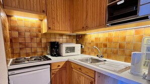 Cuina compacta amb armaris de fusta, un refrigerador blanc, microones, rentamics i una cafetera.