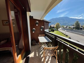 A balcony with a wooden table and chair, potted plants, and a view of a mountain landscape.
