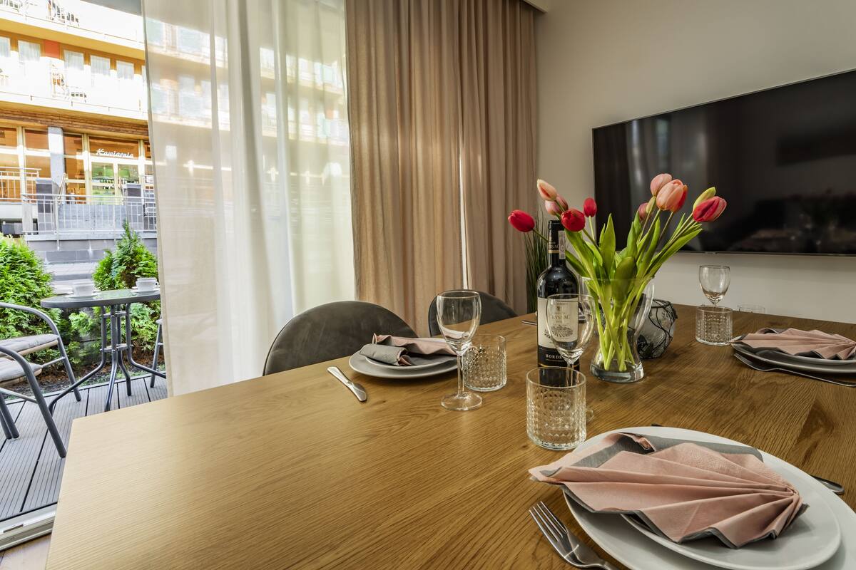 Een eettafel gedekt met borden, bestek en glazen, met een fles wijn en een vaas tulpen.