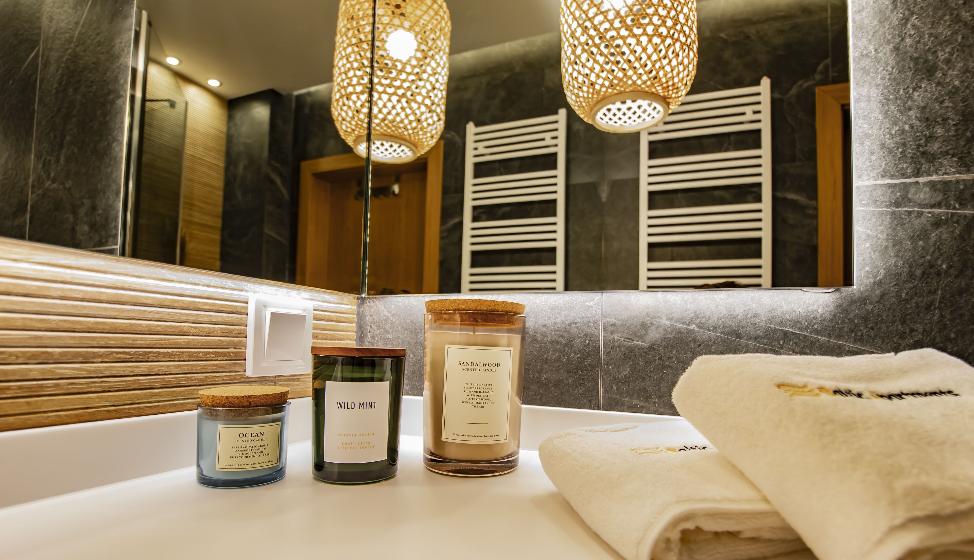A bathroom with a marble countertop, three scented candles, and a towel.