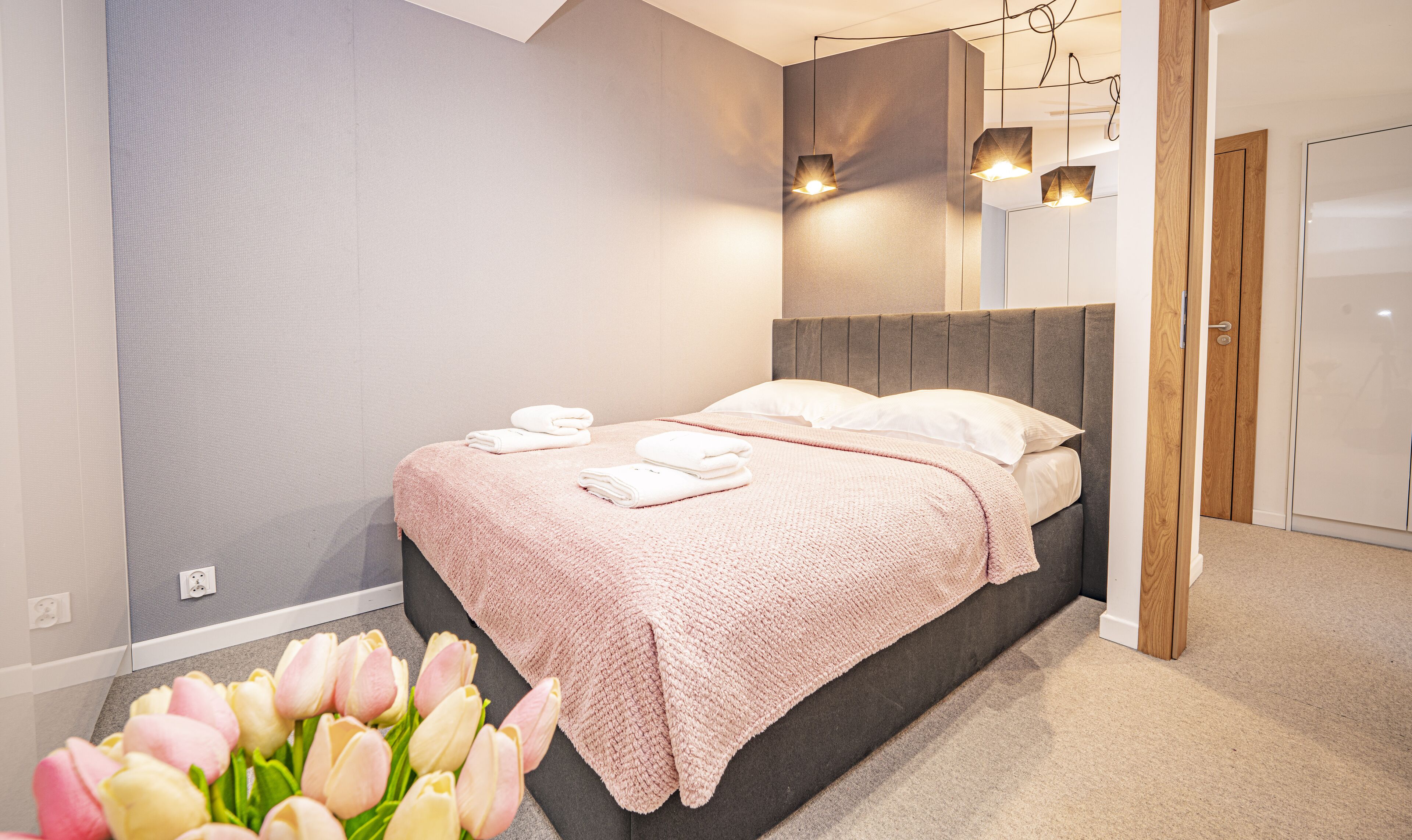 A modern bedroom with a bed, bedside lamps, and a bouquet of tulips.