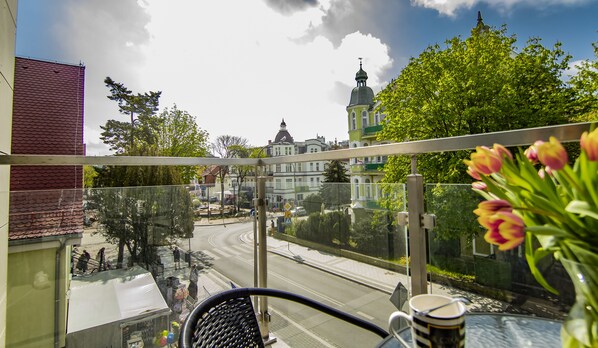 A balcony with a view of a street, a church, and a flower vase.