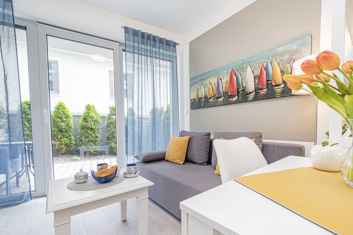 Een moderne woonkamer met een grijze bank, een witte salontafel en een schilderij van zeilboten aan de muur.