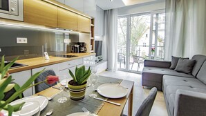 Un salon moderne avec un canapé gris, une table à manger dressée avec des assiettes et des couverts, et un coin cuisine doté de meubles en bois et d’une machine à café.