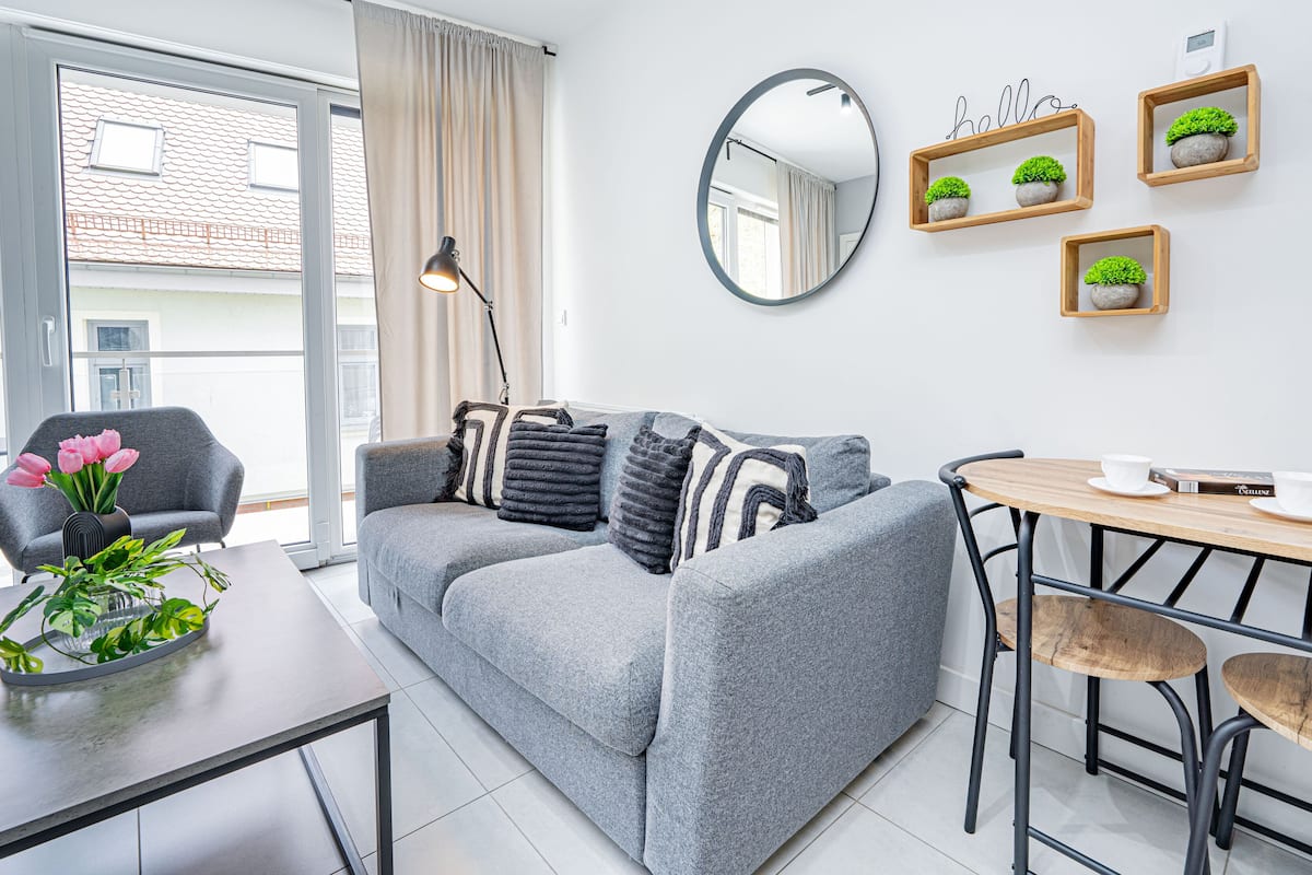 Een moderne woonkamer met een grijze bank, een houten eettafel en een spiegel aan de muur.