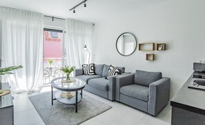 A modern living room with a grey sofa, a round coffee table, and a large window with white curtains.