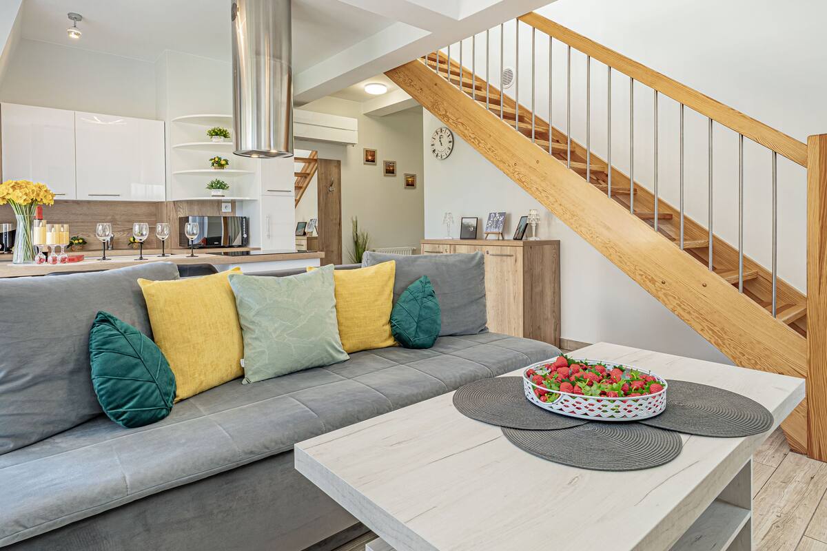 Een moderne woonkamer met een grijze bank, een salontafel met een fruitschaal, en een houten trap.